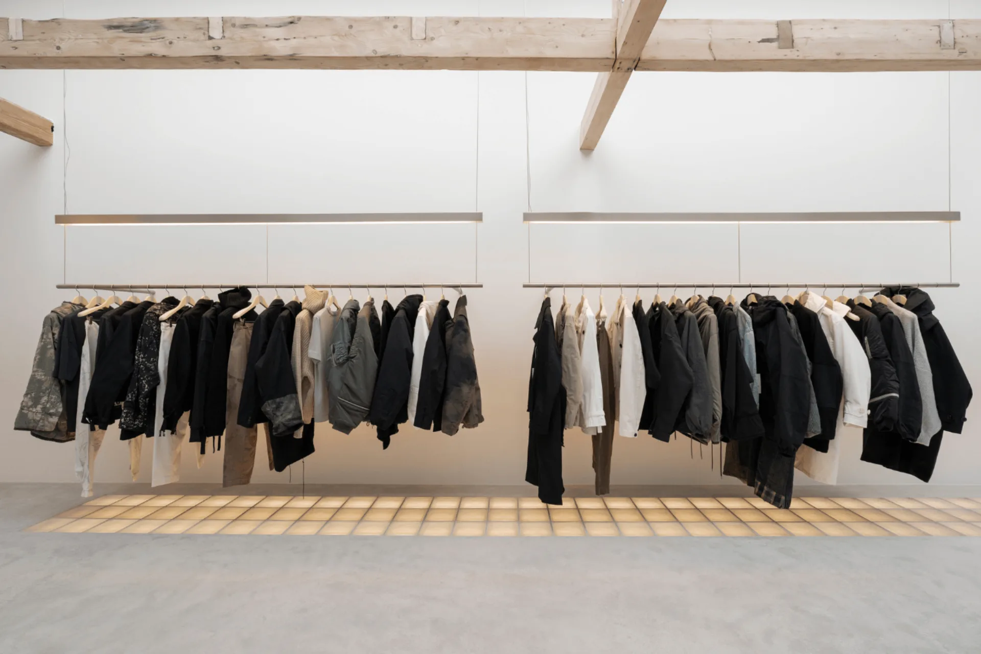 Kledingrekken op houten platform grenzend aan microcement vloer in concept store