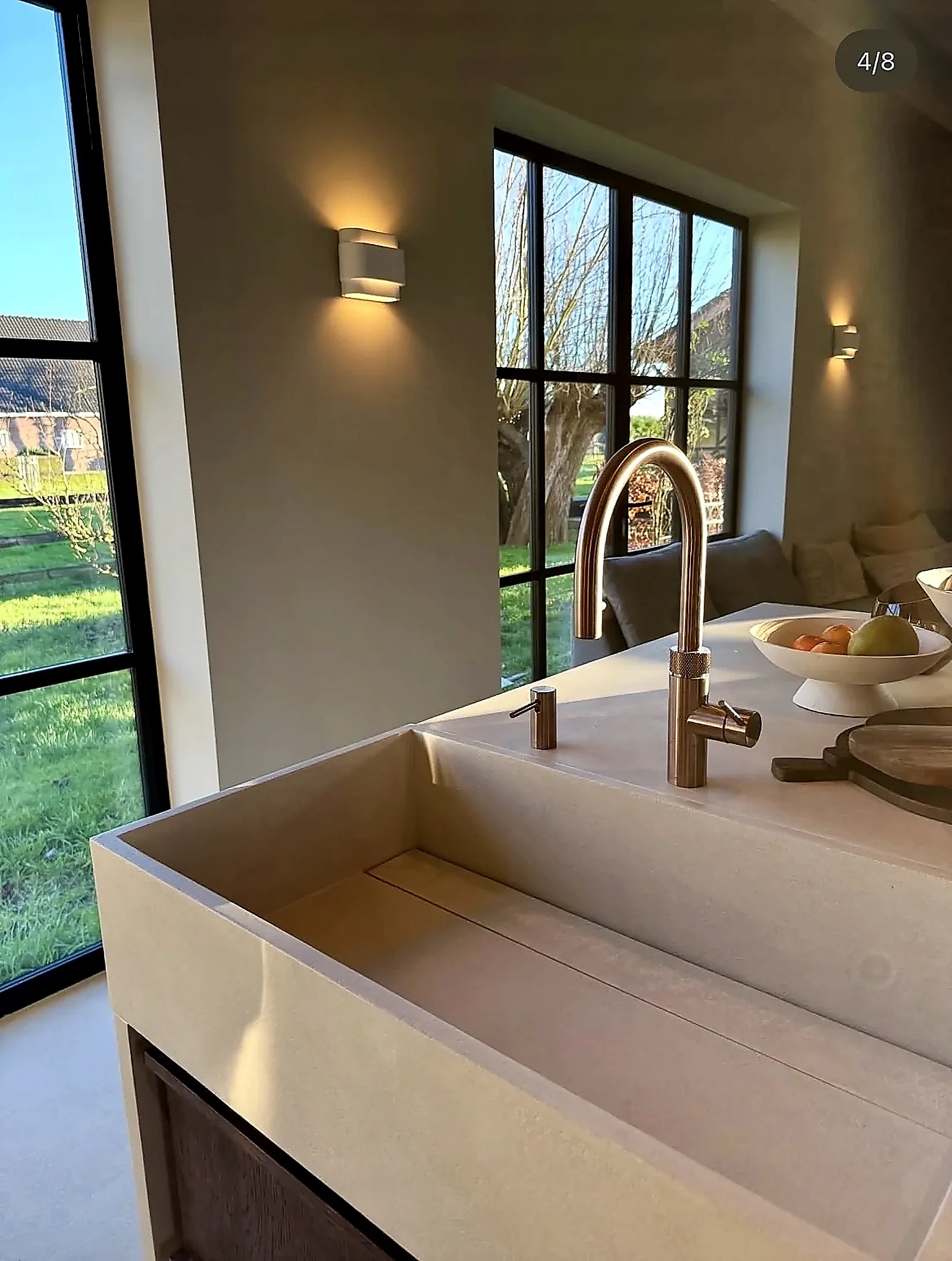 Detail van microcement spoelbak met koperen kraan en uitzicht op tuin in woonboerderij